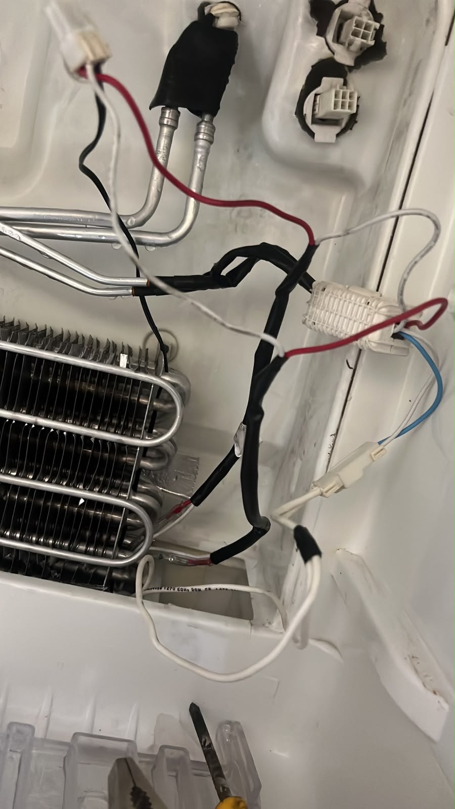Tubulações e conexões internas de uma geladeira durante reparo técnico